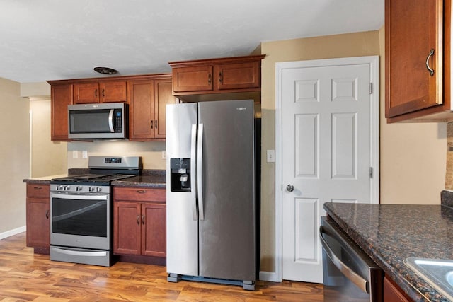 kitchen featuring stainless steel appliances, dark stone counters, and light hardwood / wood-style flooring