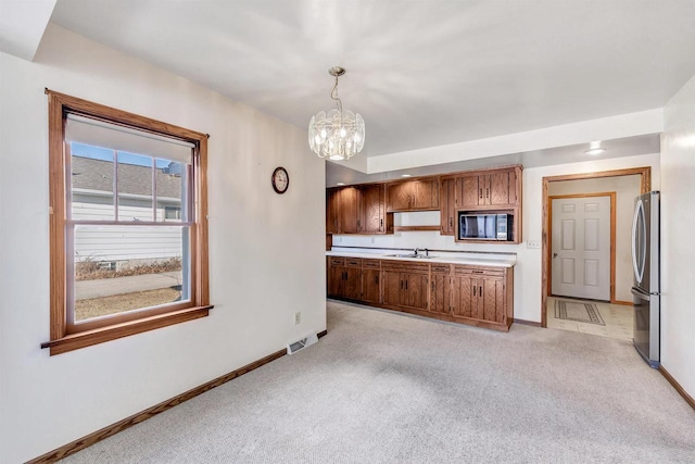 kitchen with sink, black microwave, stainless steel refrigerator, pendant lighting, and light colored carpet