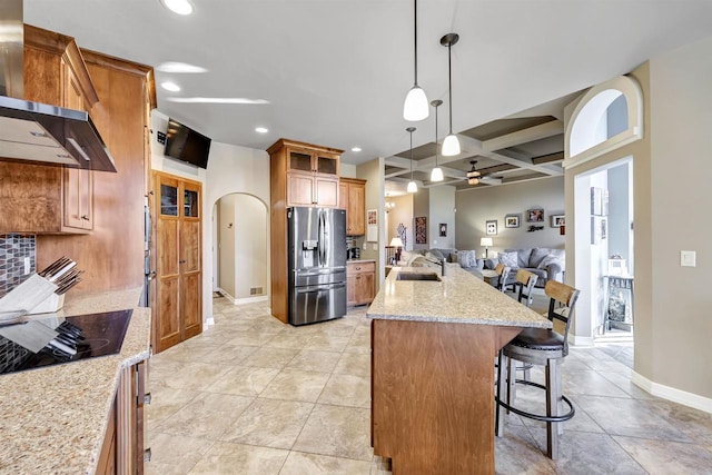 kitchen featuring pendant lighting, sink, wall chimney range hood, stainless steel refrigerator with ice dispenser, and coffered ceiling