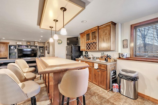 kitchen with black refrigerator, hanging light fixtures, sink, and a breakfast bar