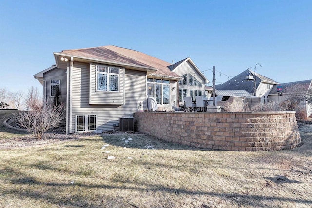 rear view of house with central AC unit and a lawn