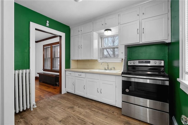 kitchen with stainless steel range with electric stovetop, radiator, white cabinetry, and sink