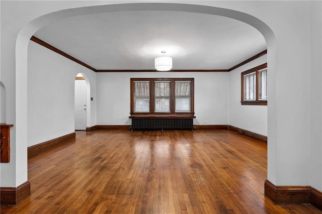 unfurnished living room with hardwood / wood-style floors, crown molding, and radiator heating unit