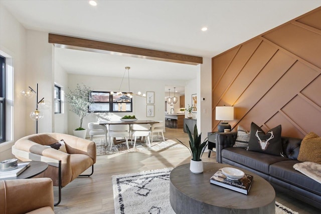 living room featuring beam ceiling, an inviting chandelier, and light hardwood / wood-style flooring