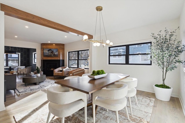 dining area with a fireplace, beam ceiling, a chandelier, and light wood-type flooring