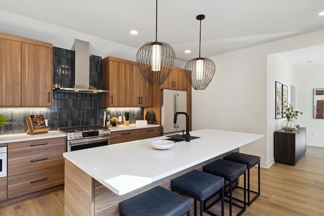 kitchen with high quality appliances, a kitchen island with sink, a kitchen breakfast bar, and wall chimney exhaust hood