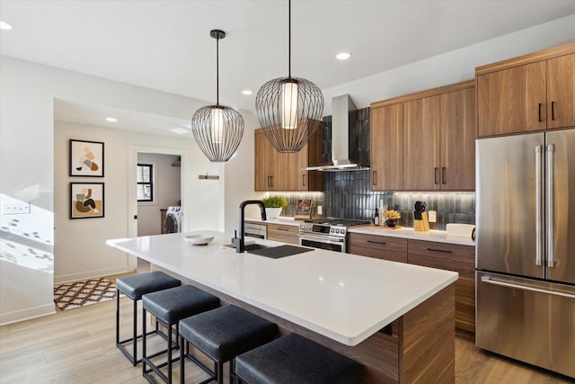 kitchen featuring wall chimney range hood, sink, backsplash, high quality appliances, and an island with sink