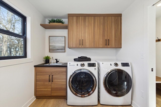 clothes washing area with cabinets, light hardwood / wood-style floors, sink, and washer and dryer