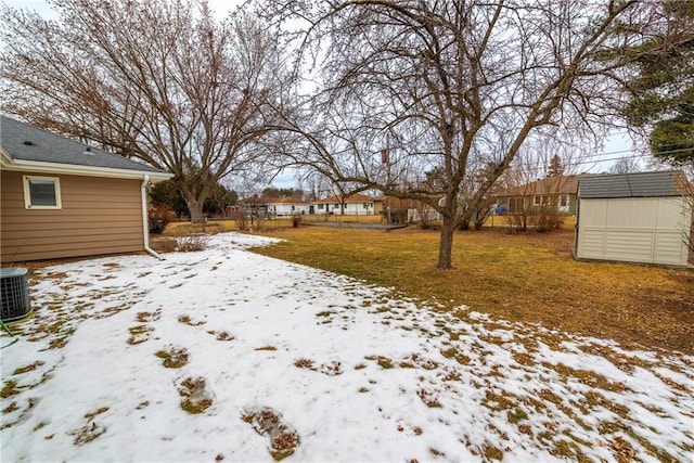 yard layered in snow featuring cooling unit and a storage shed