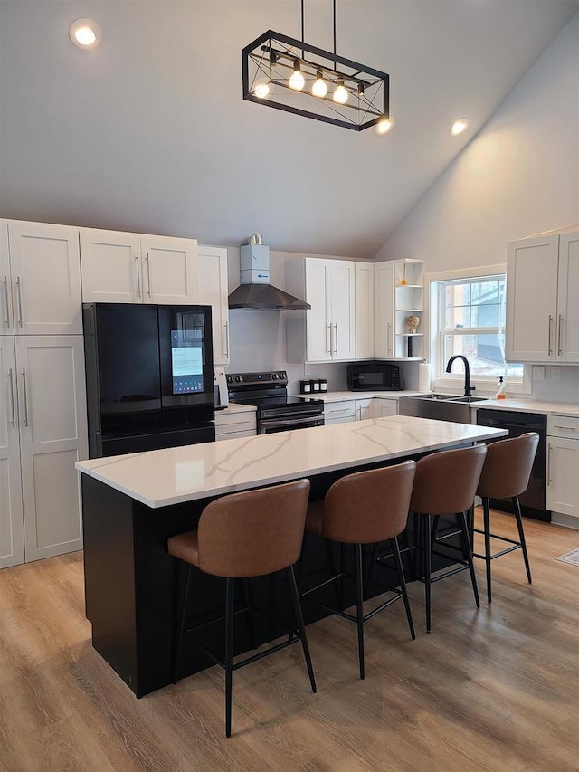 kitchen featuring wall chimney exhaust hood, white cabinetry, a center island, hanging light fixtures, and black appliances