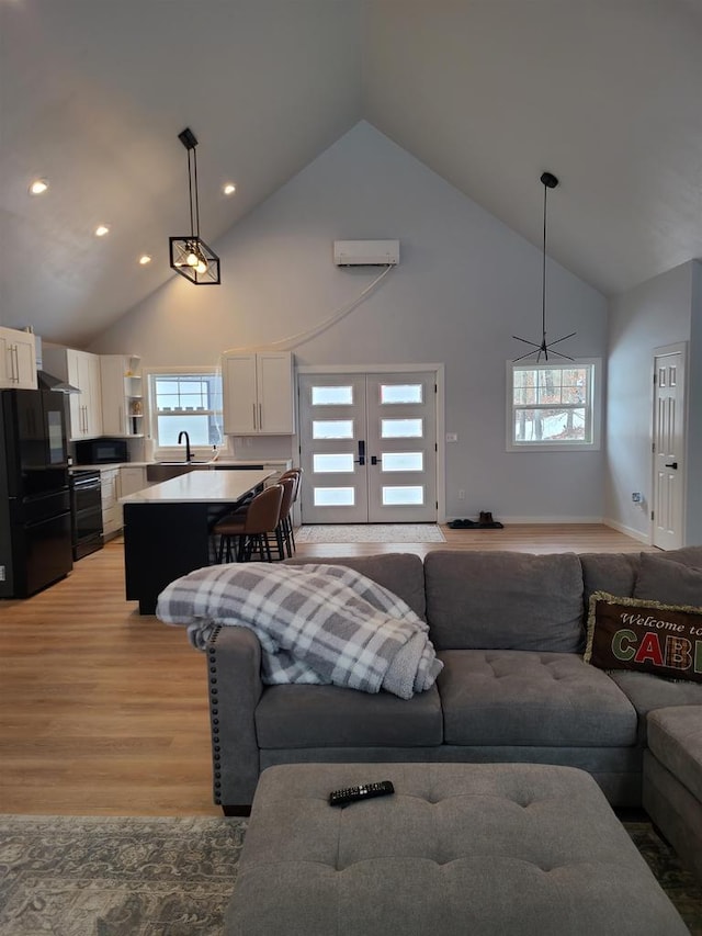 living room with high vaulted ceiling, sink, a wall unit AC, light wood-type flooring, and french doors