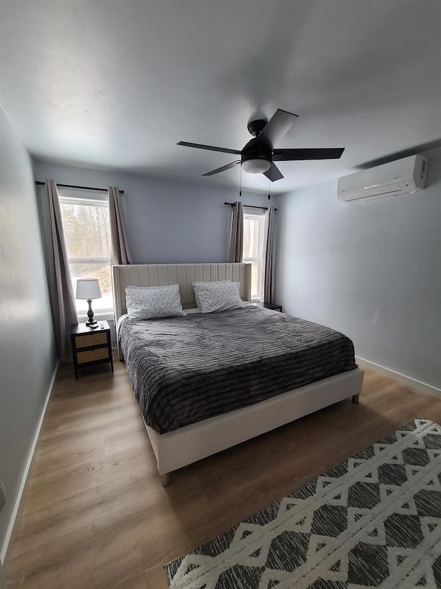 bedroom with a wall mounted AC, light hardwood / wood-style floors, and multiple windows