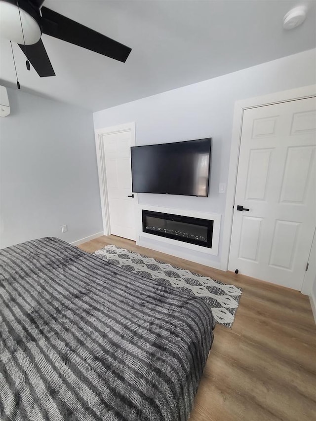 bedroom with ceiling fan, wood-type flooring, and a wall mounted air conditioner