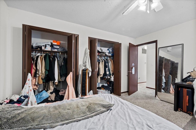 carpeted bedroom with ceiling fan, two closets, and a textured ceiling