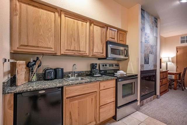 kitchen with sink, a tile fireplace, appliances with stainless steel finishes, light carpet, and dark stone counters