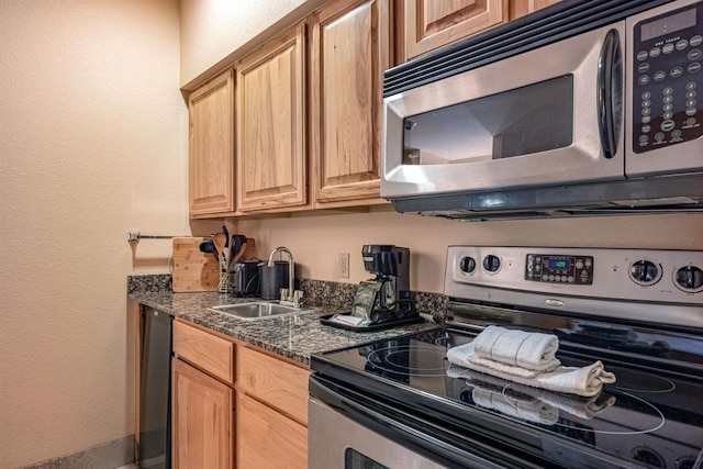 kitchen with appliances with stainless steel finishes, sink, and dark stone counters