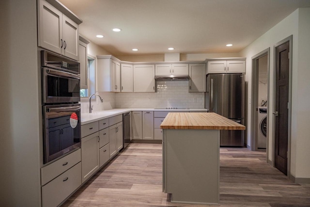 kitchen featuring butcher block countertops, washer / dryer, sink, a center island, and stainless steel appliances