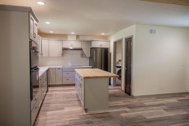 kitchen with stainless steel fridge, butcher block counters, tasteful backsplash, a kitchen island, and black electric cooktop