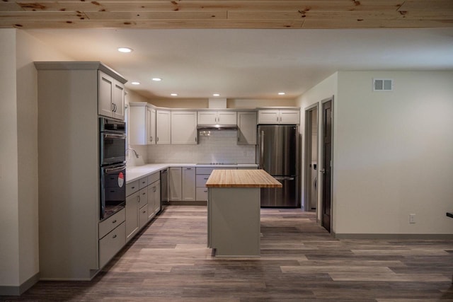 kitchen with wood counters, wood-type flooring, a center island, decorative backsplash, and black appliances