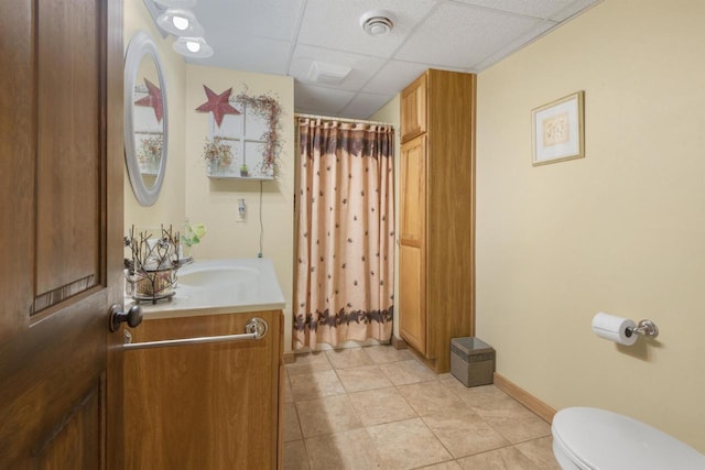 bathroom with vanity, toilet, tile patterned flooring, and a drop ceiling