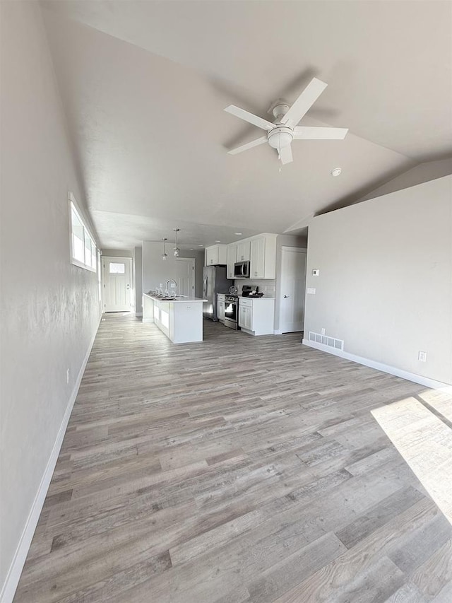 unfurnished living room featuring lofted ceiling, sink, light hardwood / wood-style floors, and ceiling fan