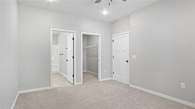 unfurnished bedroom with a spacious closet, light colored carpet, ceiling fan, ensuite bath, and a closet