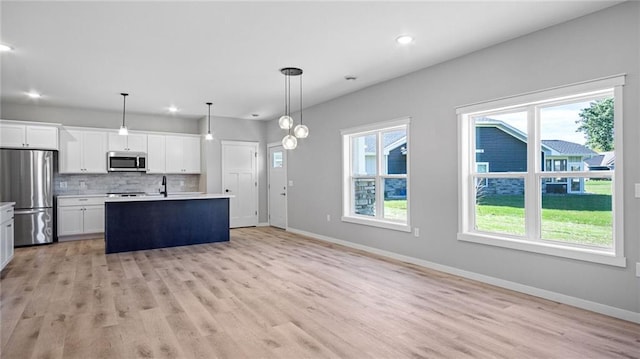 kitchen featuring appliances with stainless steel finishes, white cabinets, backsplash, hanging light fixtures, and a kitchen island with sink