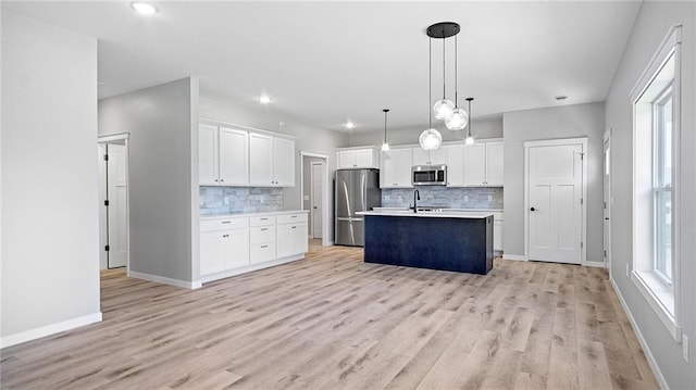 kitchen with stainless steel appliances, an island with sink, pendant lighting, and white cabinets