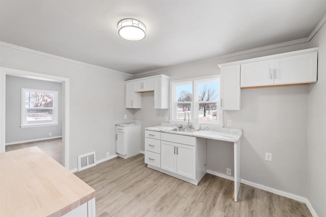 kitchen with white cabinetry, ornamental molding, light hardwood / wood-style floors, and sink