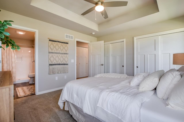 carpeted bedroom with a raised ceiling, ensuite bathroom, two closets, and ceiling fan