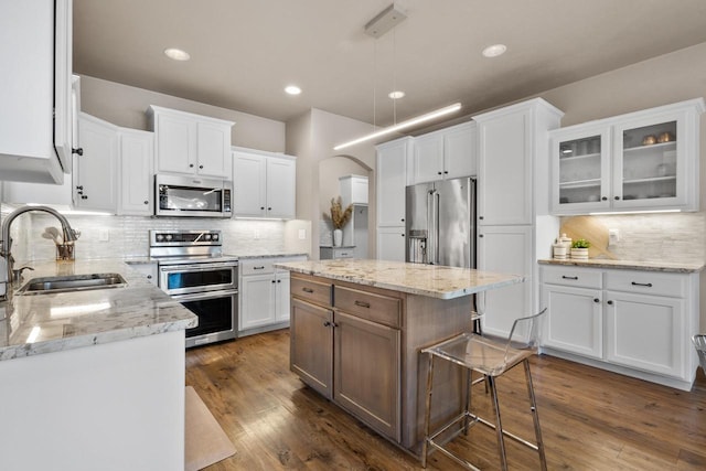 kitchen with a kitchen island, appliances with stainless steel finishes, white cabinetry, sink, and light stone counters