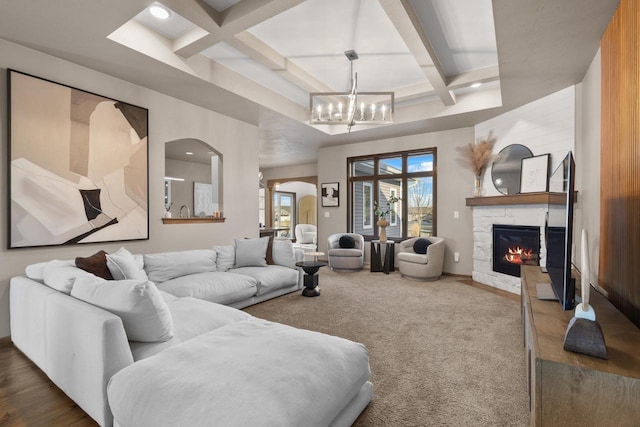 carpeted living room with coffered ceiling, a stone fireplace, beam ceiling, and an inviting chandelier