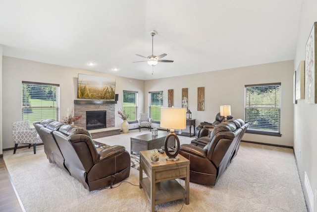 living room featuring ceiling fan, a stone fireplace, and a healthy amount of sunlight