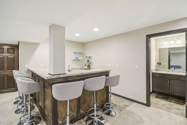 bar with dark brown cabinetry, light carpet, and light stone countertops