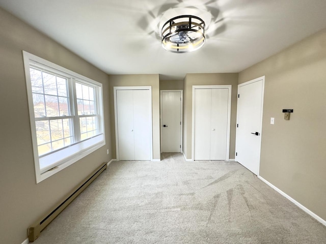 unfurnished bedroom with baseboard heating, multiple closets, and light carpet