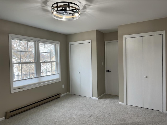 unfurnished bedroom with multiple closets, light colored carpet, and baseboard heating