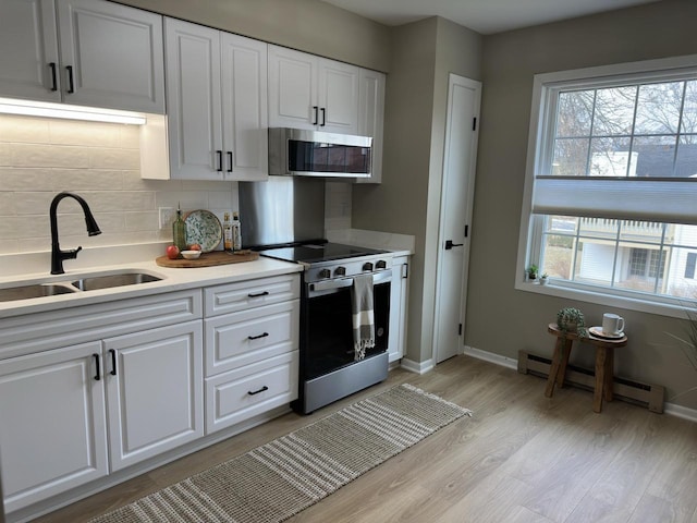 kitchen featuring white cabinetry, a baseboard heating unit, sink, and appliances with stainless steel finishes