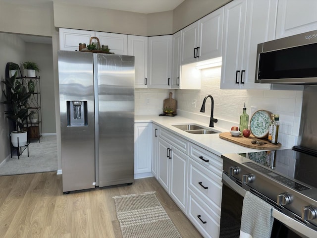 kitchen with appliances with stainless steel finishes, tasteful backsplash, sink, white cabinets, and light hardwood / wood-style floors