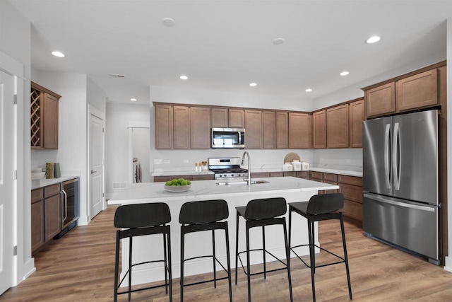 kitchen featuring sink, a breakfast bar area, stainless steel appliances, an island with sink, and light wood-type flooring