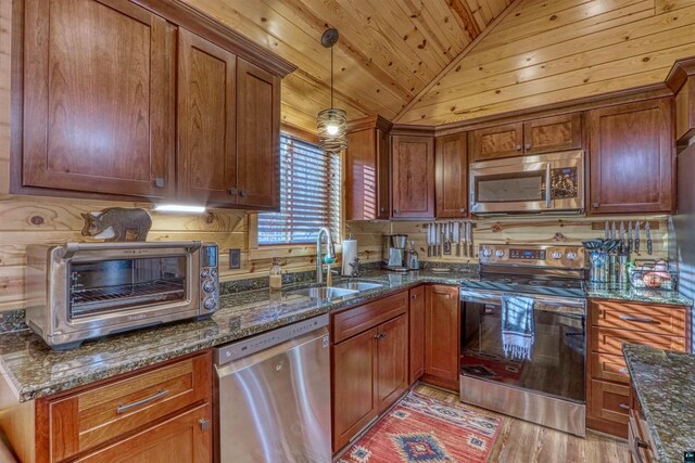 kitchen with appliances with stainless steel finishes, pendant lighting, lofted ceiling, sink, and dark stone countertops