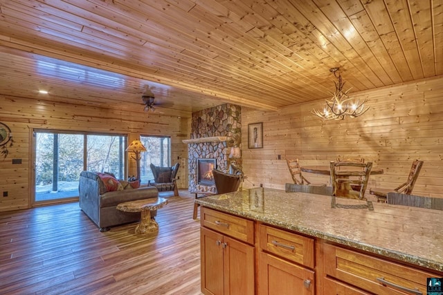 kitchen featuring light stone counters, wood ceiling, decorative light fixtures, light wood-type flooring, and wooden walls