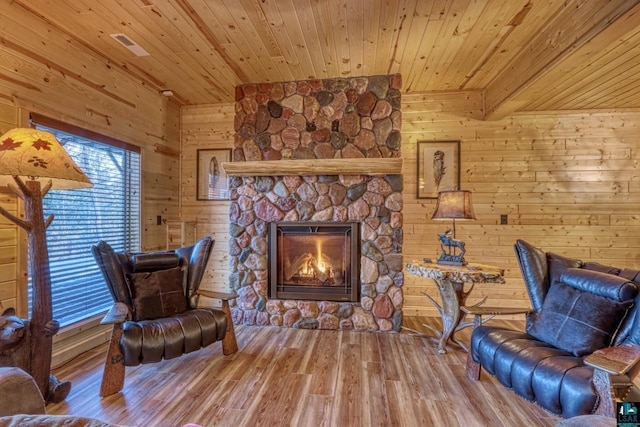 sitting room featuring a stone fireplace, hardwood / wood-style floors, wooden ceiling, and wood walls