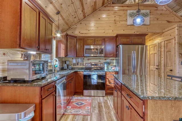 kitchen with sink, hanging light fixtures, dark stone countertops, stainless steel appliances, and light hardwood / wood-style floors