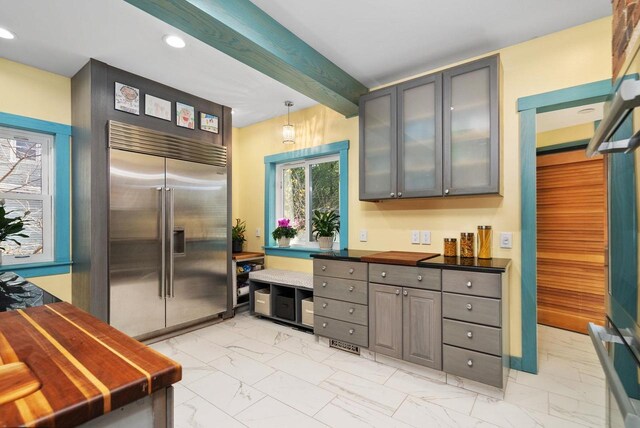 kitchen with pendant lighting, beam ceiling, stainless steel built in fridge, and gray cabinetry