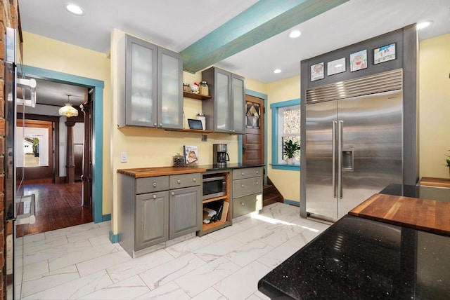 kitchen featuring gray cabinets, appliances with stainless steel finishes, butcher block counters, a wealth of natural light, and beamed ceiling