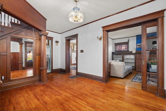 spare room featuring a notable chandelier, crown molding, light hardwood / wood-style flooring, and ornate columns