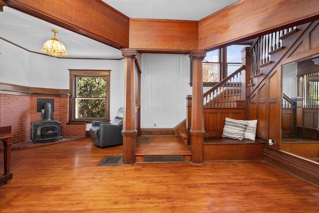 interior space featuring decorative columns, wood-type flooring, brick wall, and a wood stove