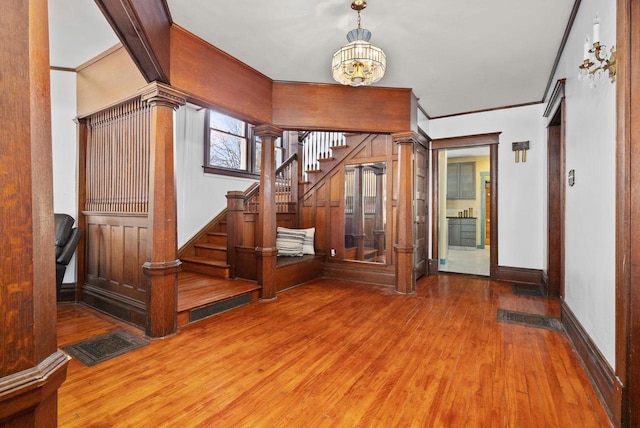 entrance foyer with an inviting chandelier, hardwood / wood-style flooring, ornamental molding, and ornate columns