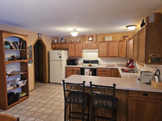 kitchen with a breakfast bar, sink, white refrigerator, kitchen peninsula, and electric stove