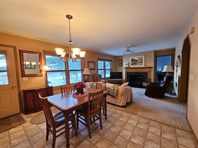 carpeted dining space featuring ceiling fan with notable chandelier, a fireplace, and a textured ceiling